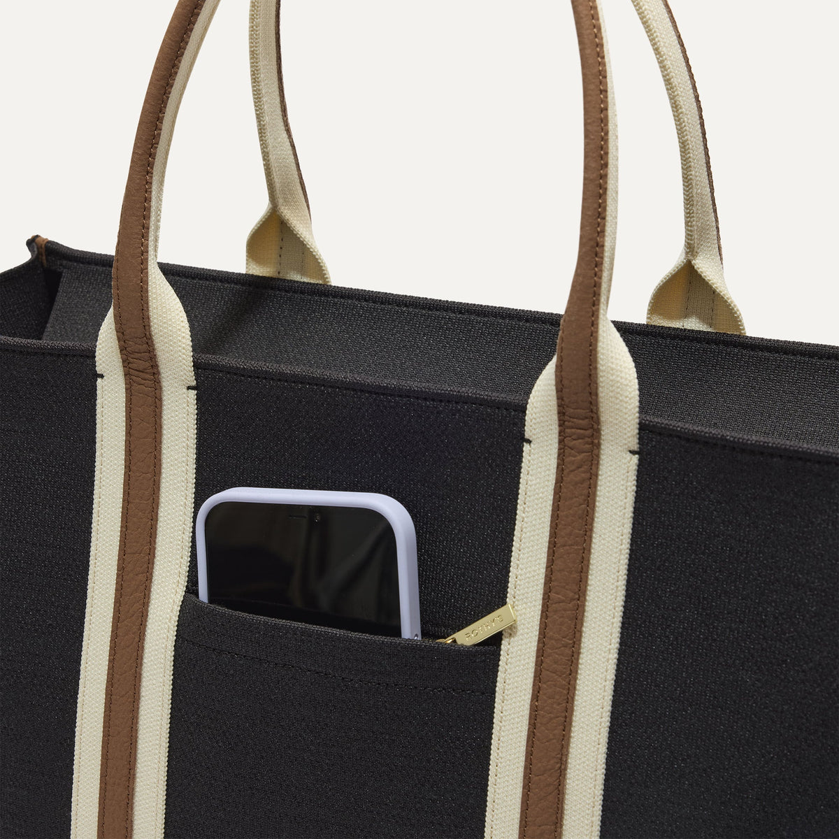 A closeup of The Classic Tote in Black Coffee, focusing on the exterior zip pocket.